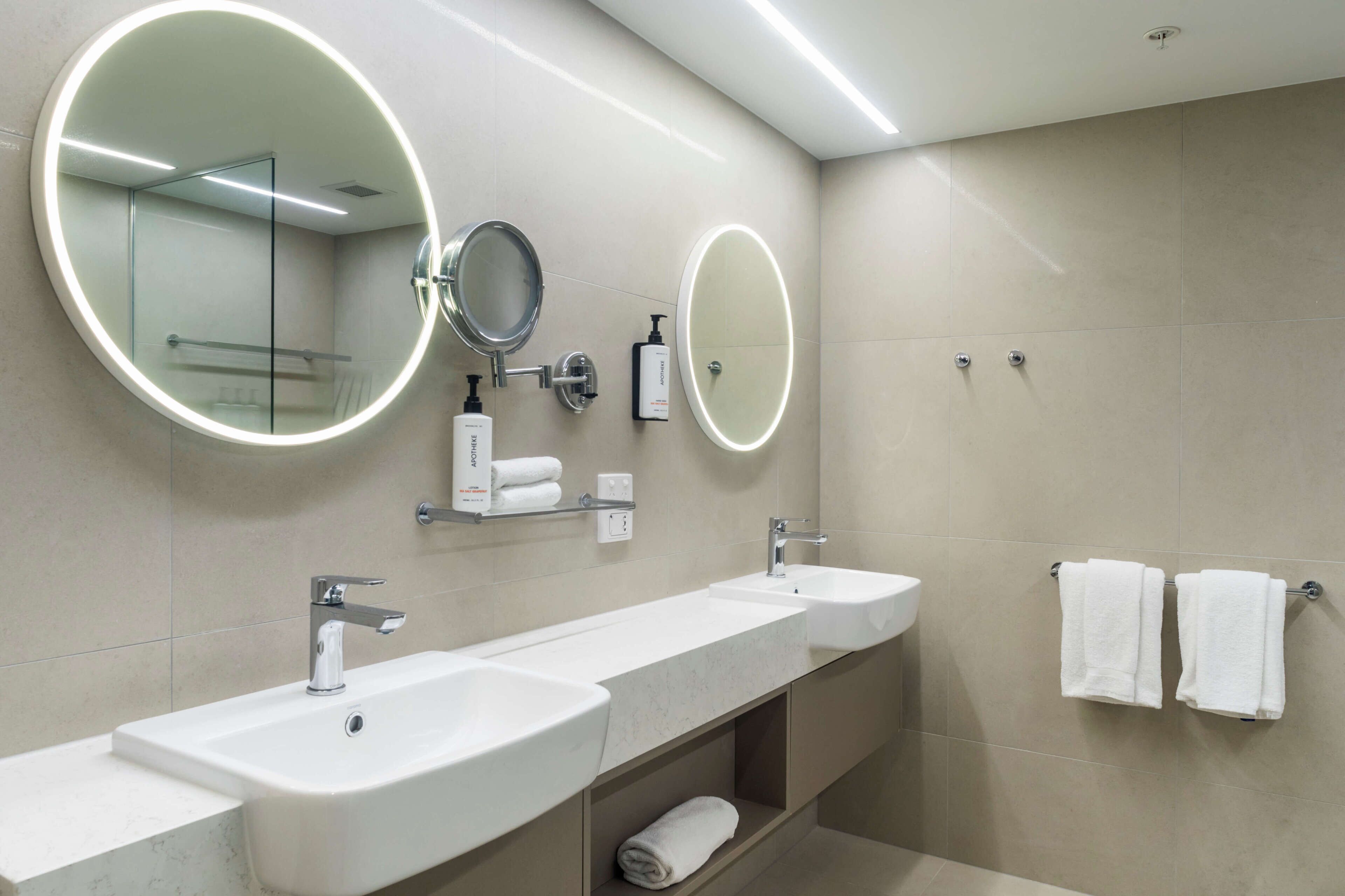 A modern bathroom with two sinks, a large mirror, and a towel rack.
