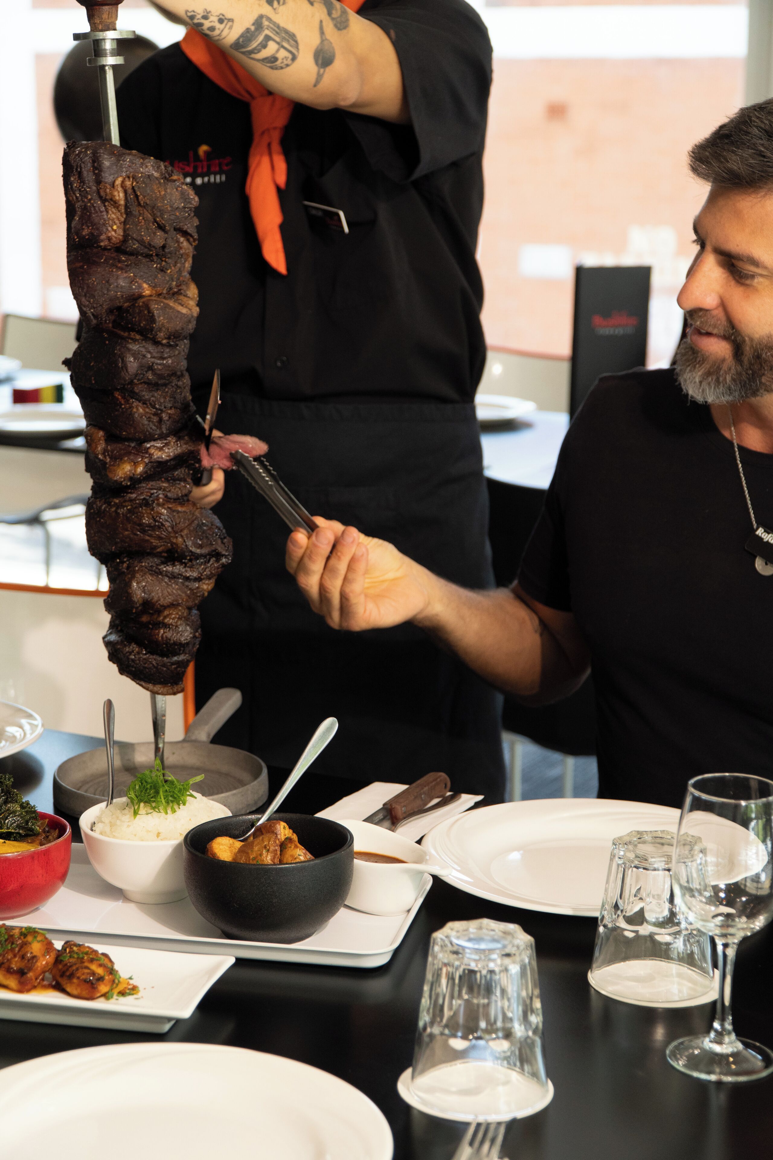 Une table dressée pour le repas, avec des brochettes de viande, des bols remplis de nourriture, ainsi que des assiettes et des verres.