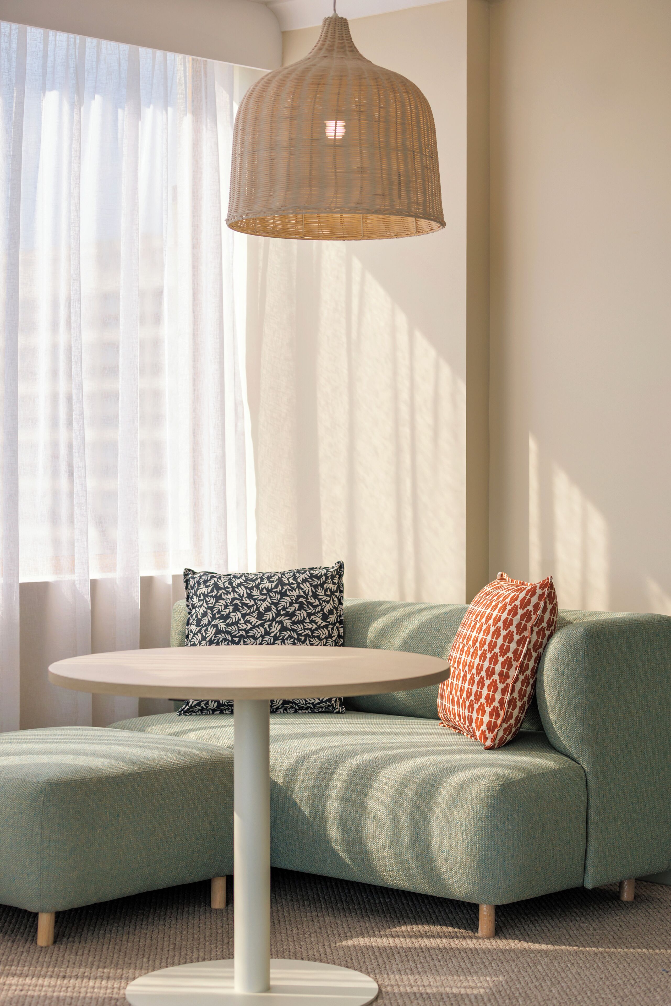 Un salon moderne avec un canapé vert, une table ronde et un luminaire suspendu en fibres tressées.