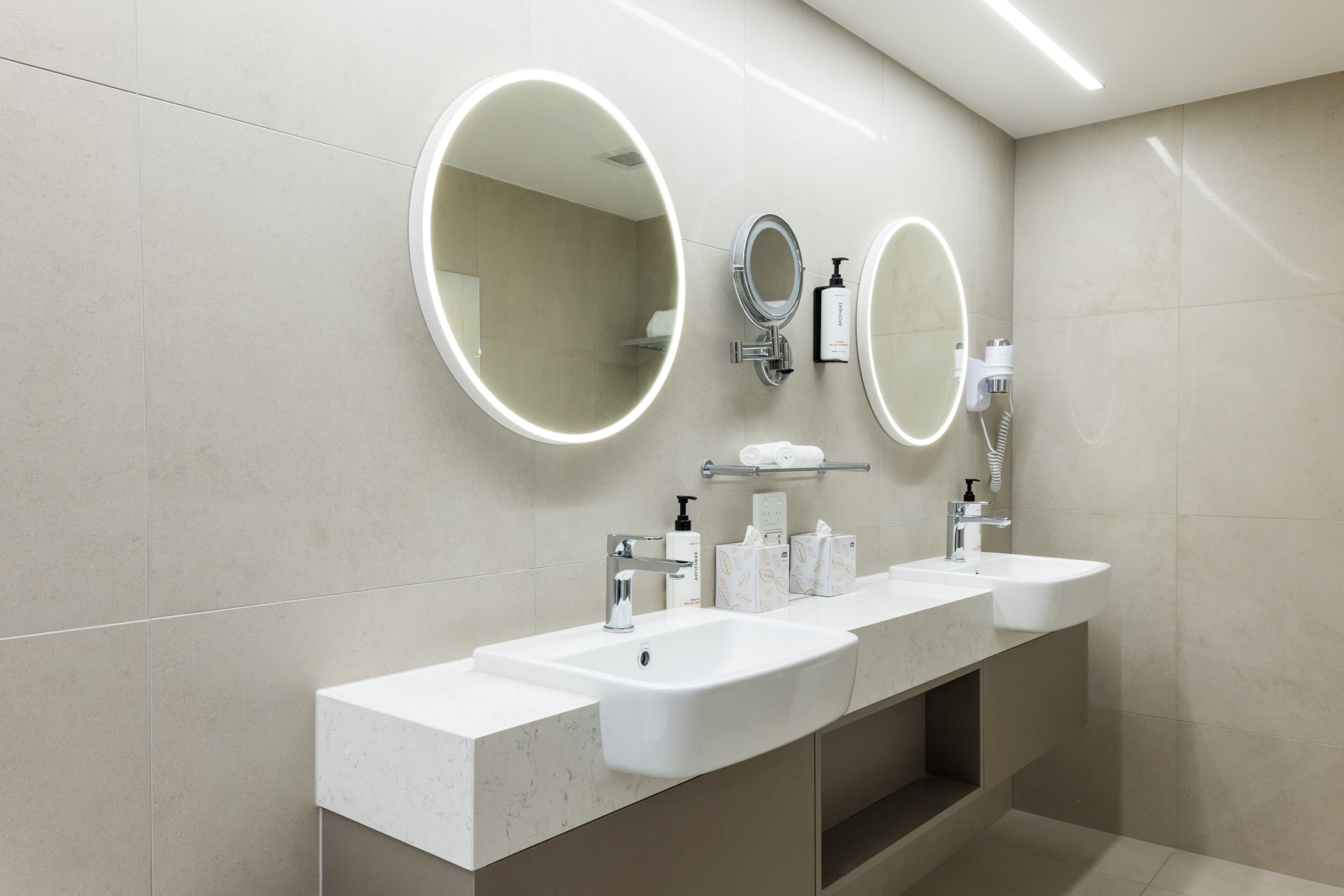 A modern bathroom with two sinks, a large mirror, and a towel rack.