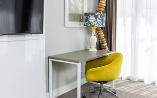 A modern office desk with a yellow chair, a white vase, and a lamp with a blue and black patterned shade.