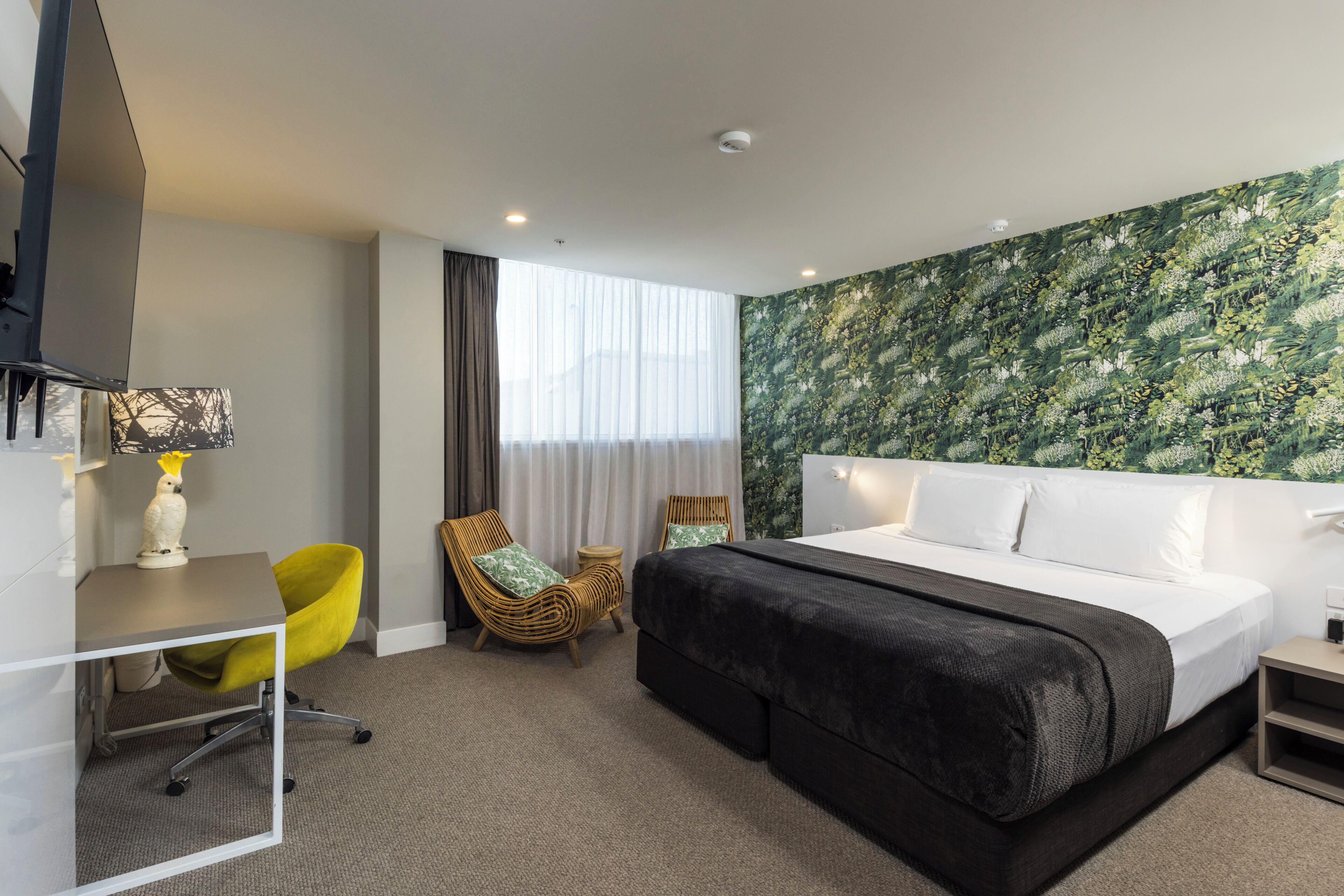 Een hotelkamer met een bed, een bureau, een stoel, een televisietoestel en een raam met gordijnen.