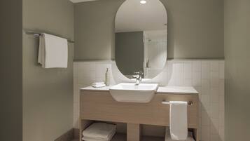 Un baño moderno con un espejo ovalado grande, un lavabo blanco y un mueble de tocador de madera.