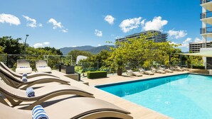 Zona de piscina con sillones de descanso y una pileta, rodeada de vegetación y vistas a montañas.