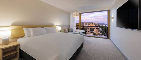 A hotel room with a large bed, a TV mounted on the wall, and a balcony with a city view.