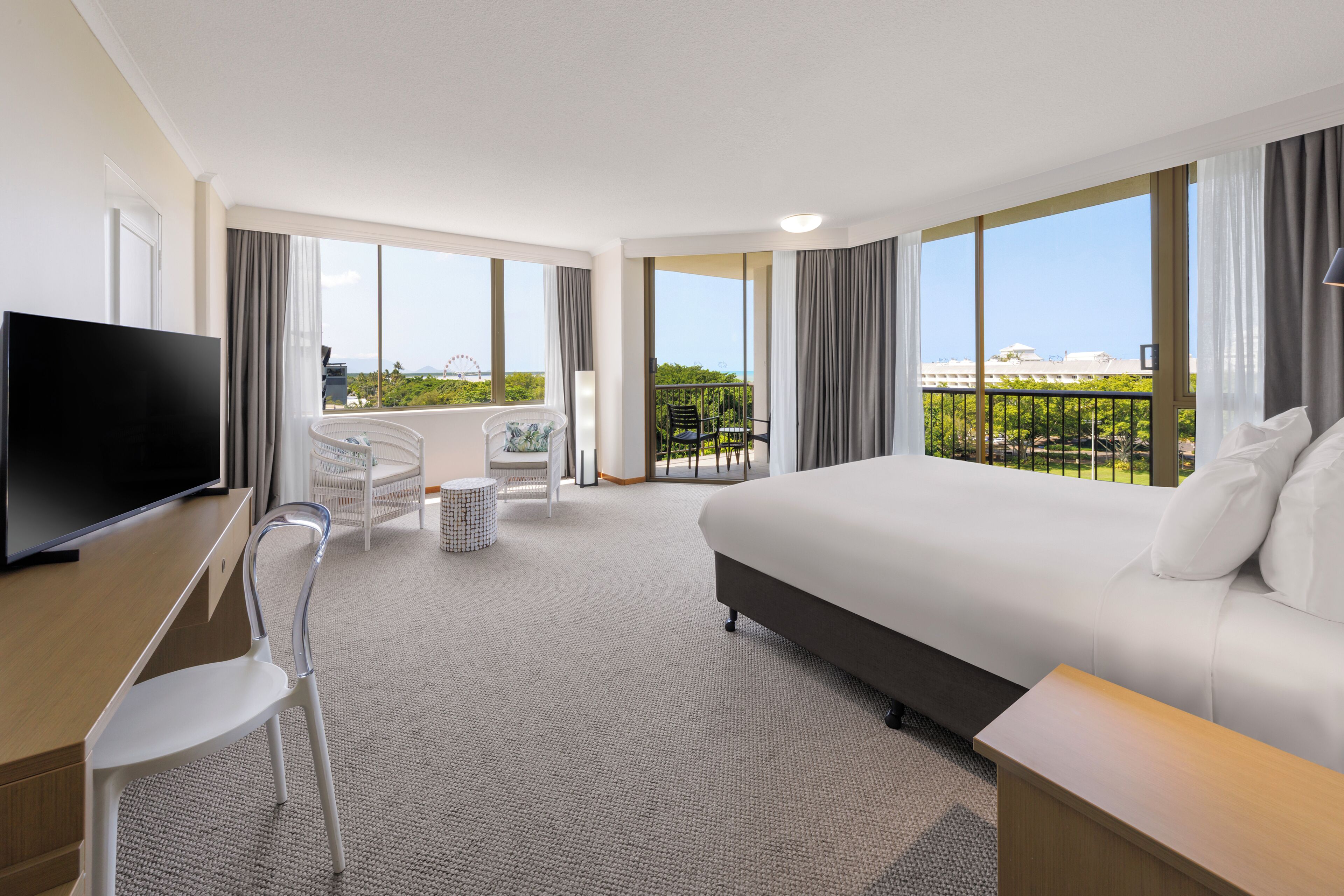 Une chambre d’hôtel équipée d’un lit, d’un bureau, d’une chaise, d’une télévision et de grandes fenêtres donnant sur la ville.