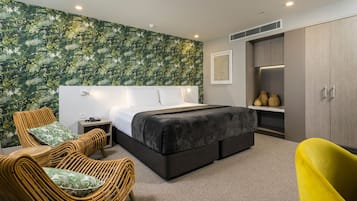 A modern bedroom with a large bed, a nightstand, a wicker chair, a yellow chair, and a wardrobe.