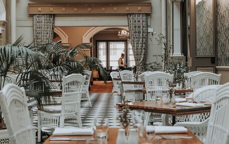 A dining area with white wicker chairs and tables, a checkered floor, and a view of a person in the background.