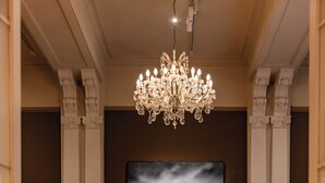 Una sala elegante con candelabro, un cuadro grande, un piano y una alfombra estampada.