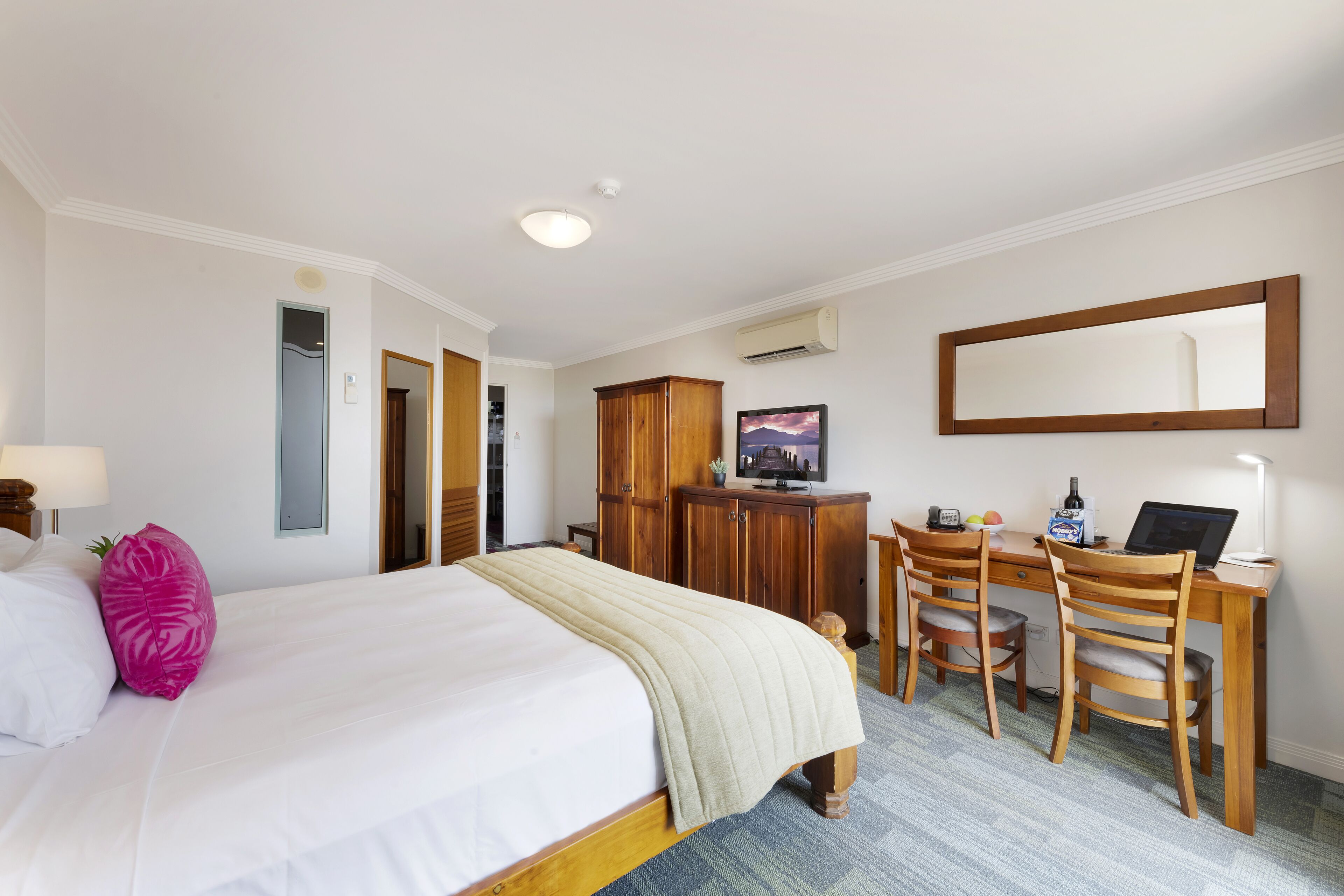 A hotel room with a bed, a desk, a chair, a mirror, and a wardrobe.