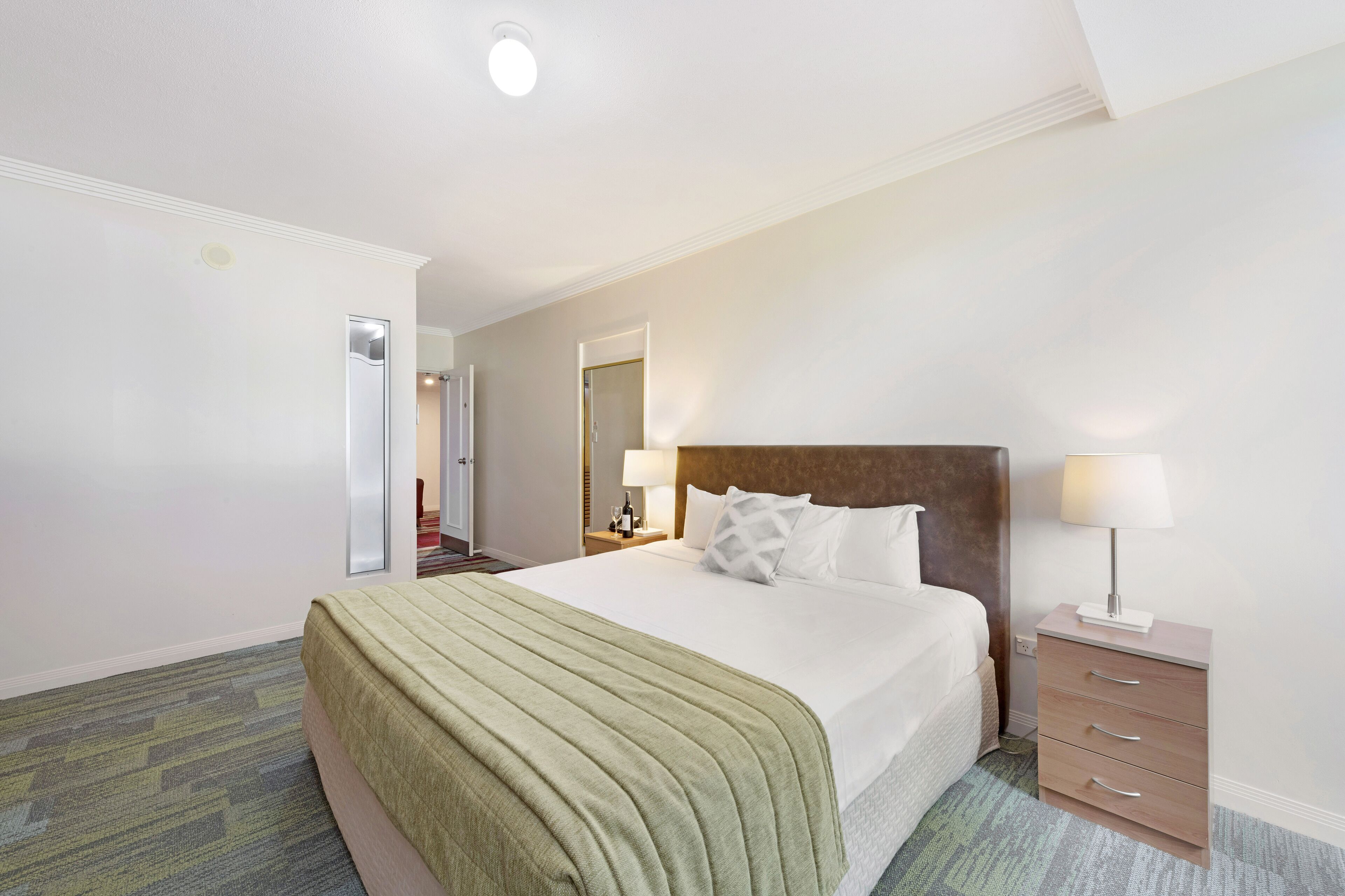 Una habitación de hotel con una cama grande, una mesita de noche con lámpara y un aparador.