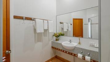 A bathroom with a white sink, a mirror, a wooden towel rack, and a small vase with flowers.
