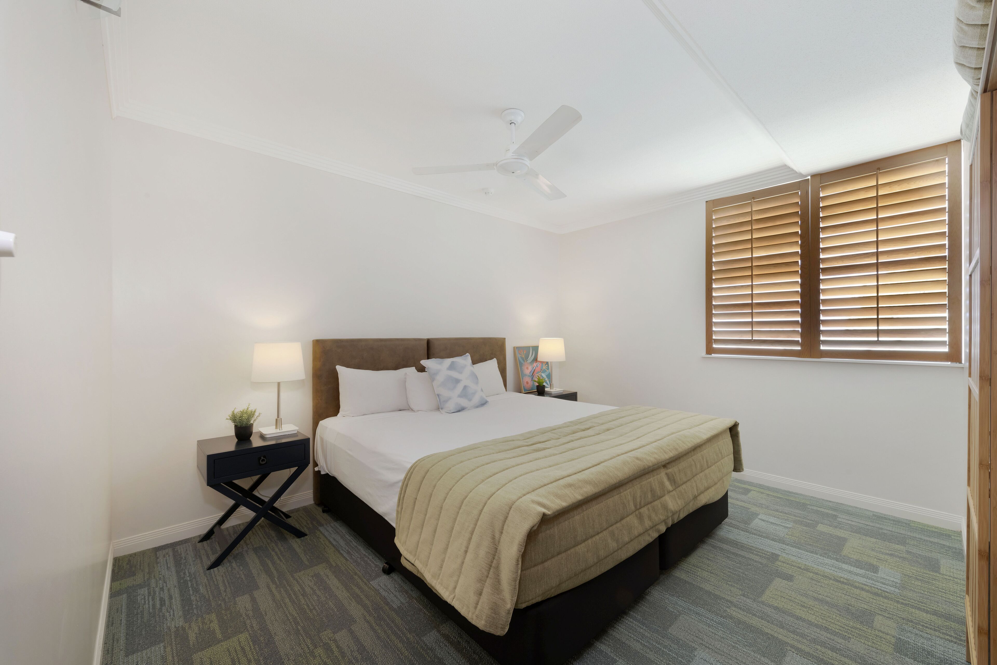A bedroom with a bed, bedside tables, a ceiling fan, and a window with blinds.
