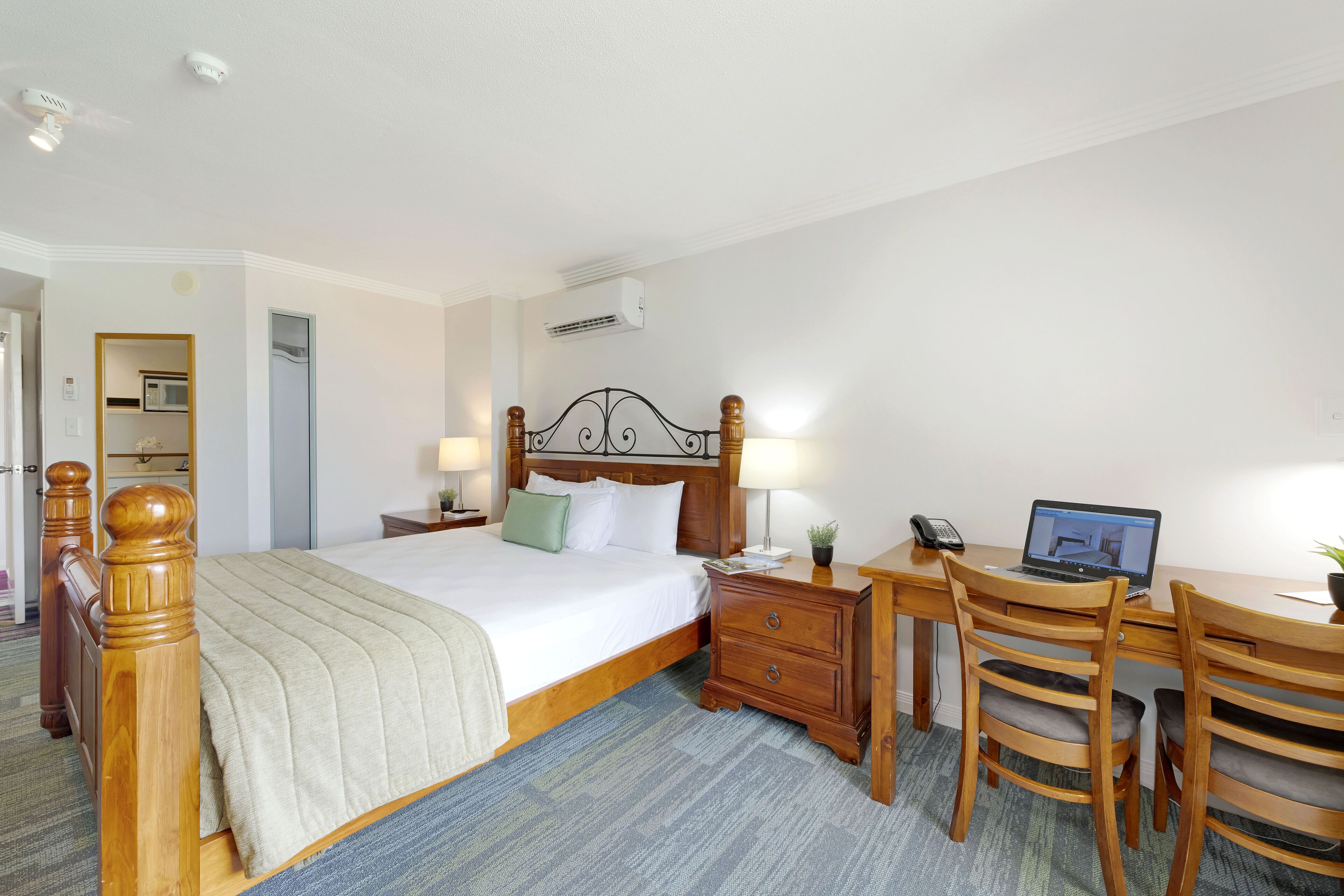 Une chambre d’hôtel avec un lit en bois, un bureau avec un ordinateur portable, un téléphone et une petite table avec une plante.