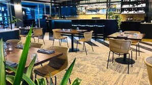 Un interior de restaurante moderno con zona de bar, mobiliario de mimbre y alfombra estampada.