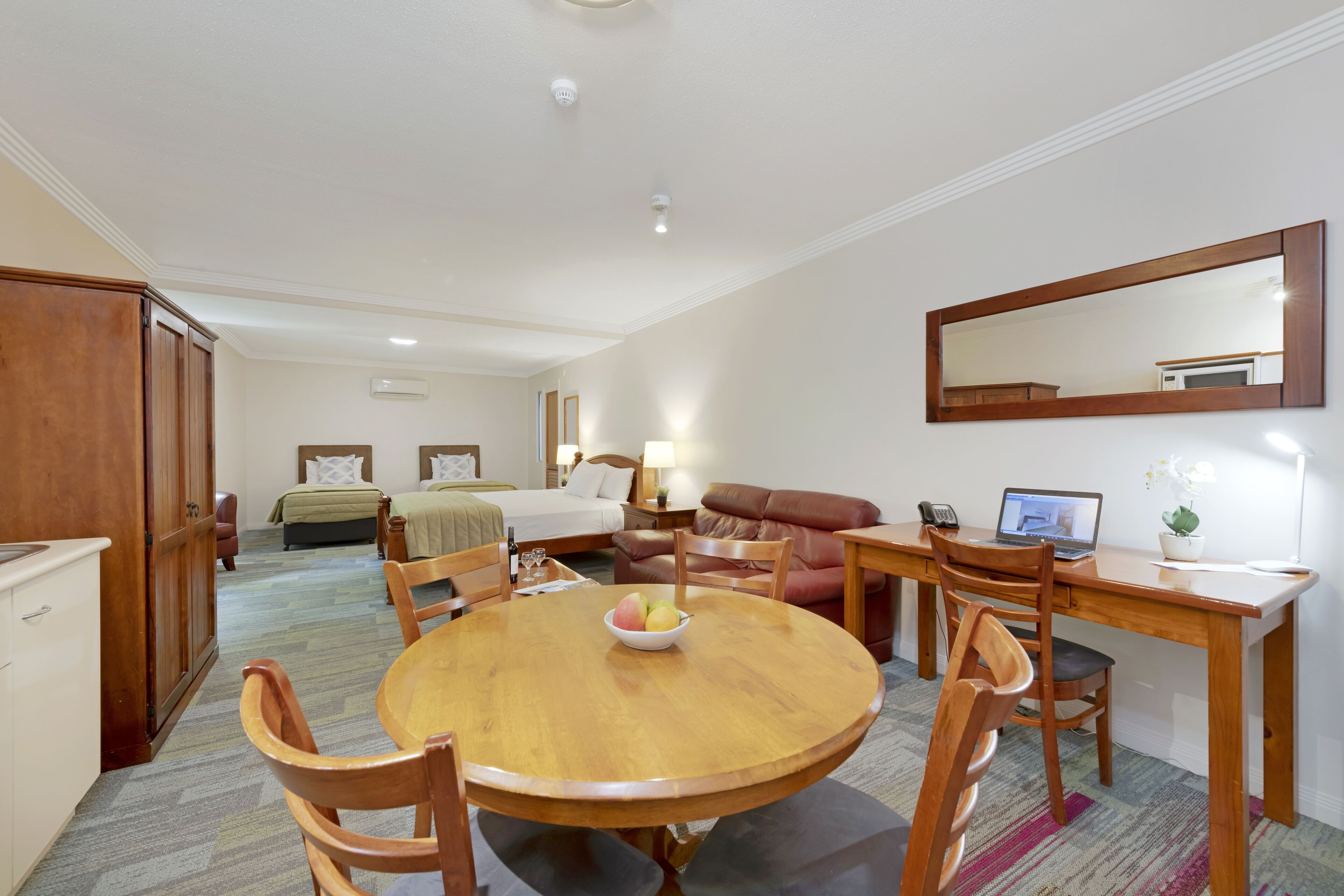 A hotel room with a bed, a desk, a dining table with chairs, a sofa, and a mirror.
