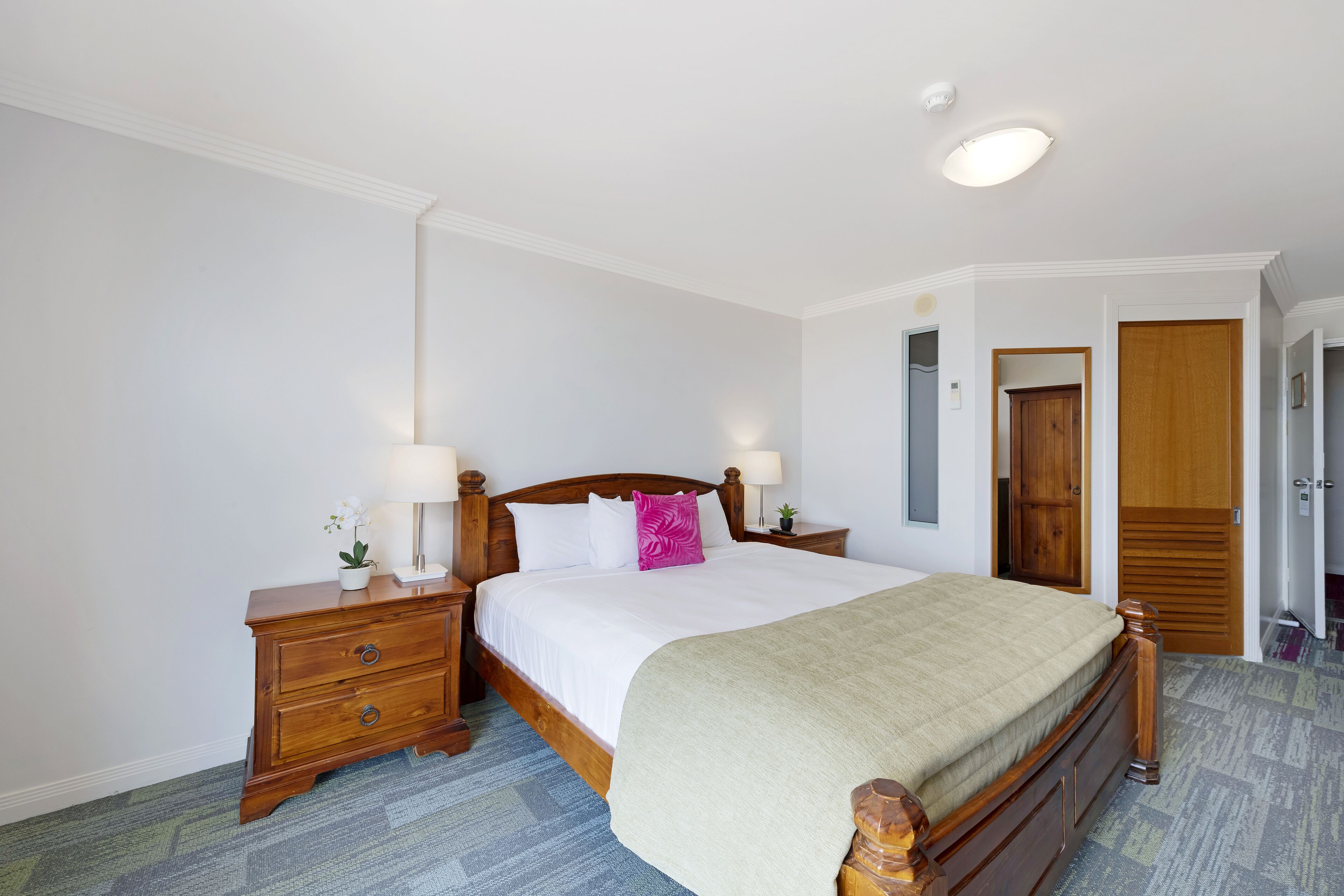 Un dormitorio ordenado con una cama de madera, dos mesitas de noche, un tocador y un armario.