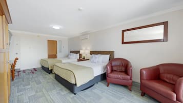 Une chambre d’hôtel avec deux lits, un fauteuil en cuir rouge, une armoire en bois et un miroir au mur.