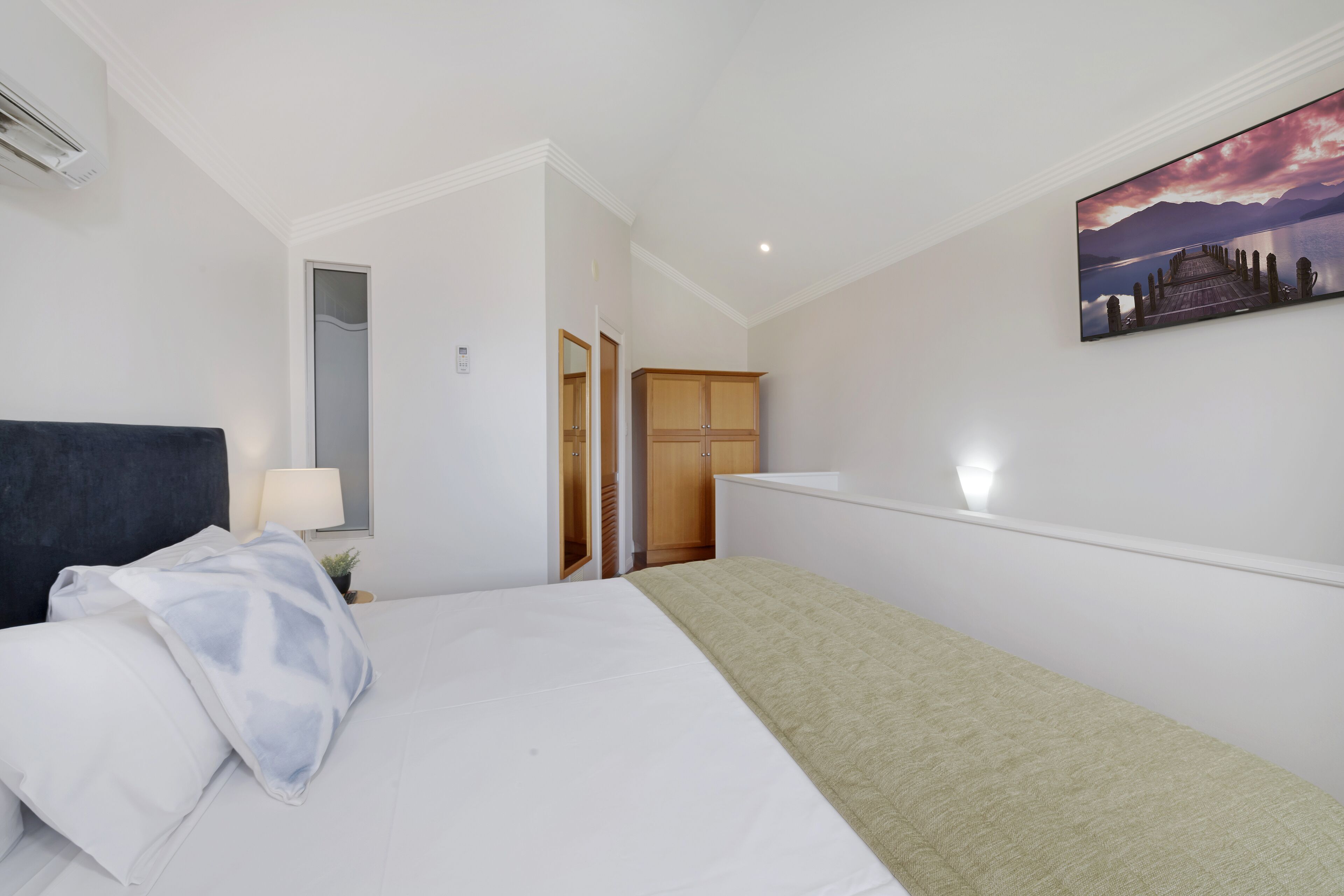 Una habitación de hotel con una cama, una lámpara de noche, un cuadro y un armario.