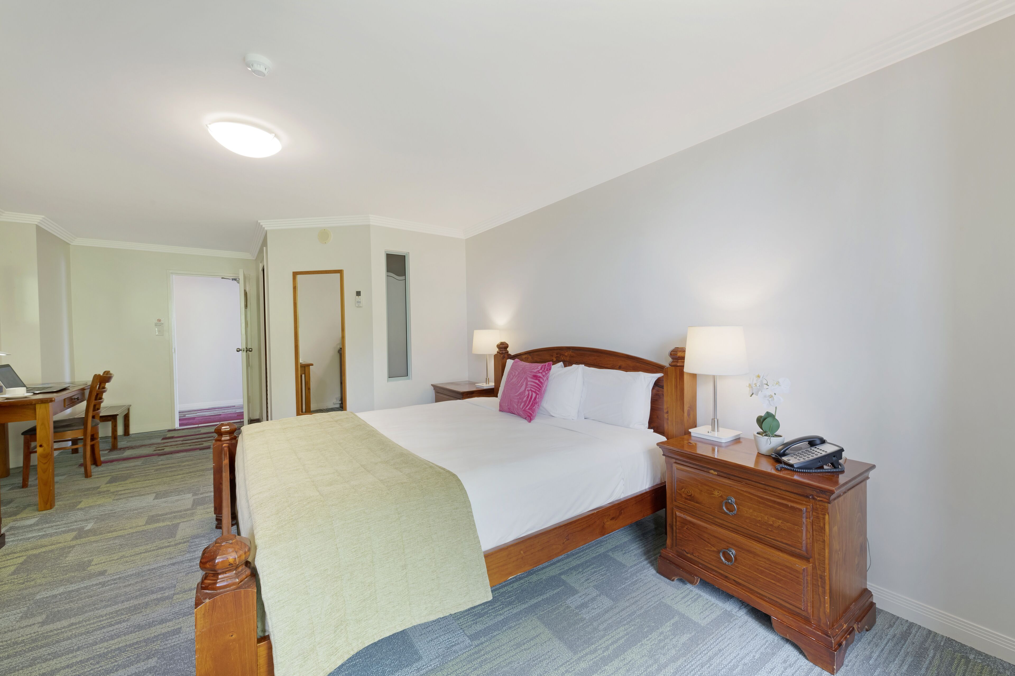 Una habitación de hotel con cama, mesita de noche, lámpara y escritorio con silla.