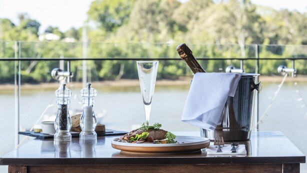 Una mesa de comedor con un plato de comida, un vaso de agua, saleros y pimenteros, una botella de champán y un portavasos.
