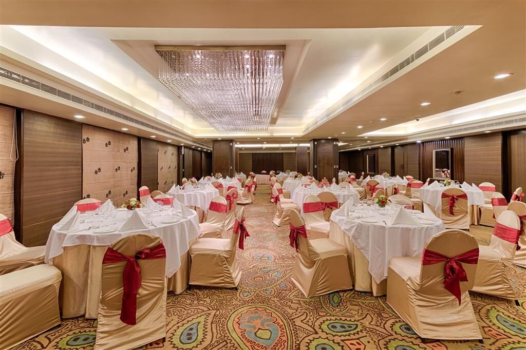 A banquet hall with round tables, chairs, and a patterned carpet.