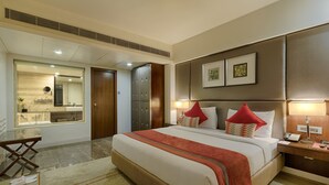 A hotel room with a large bed, a bedside table with a lamp, a mirror, and a view of the bathroom. - Quality Hotel D V Manor (Vijayawada)