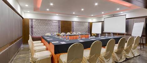 A conference room with a long table, chairs, a whiteboard, and a projector screen.