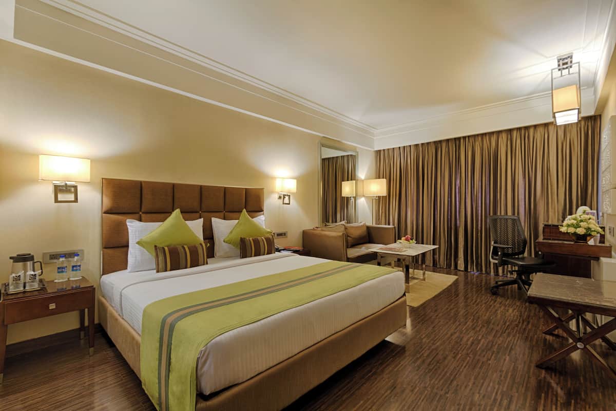 A hotel room with a large bed, a desk, a chair, a nightstand, and a lamp.