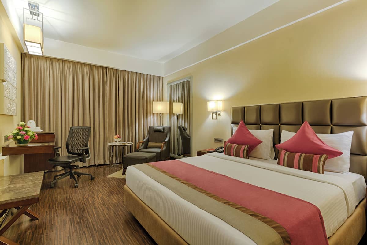 A hotel room with a large bed, two chairs, a desk, a lamp, and a nightstand.