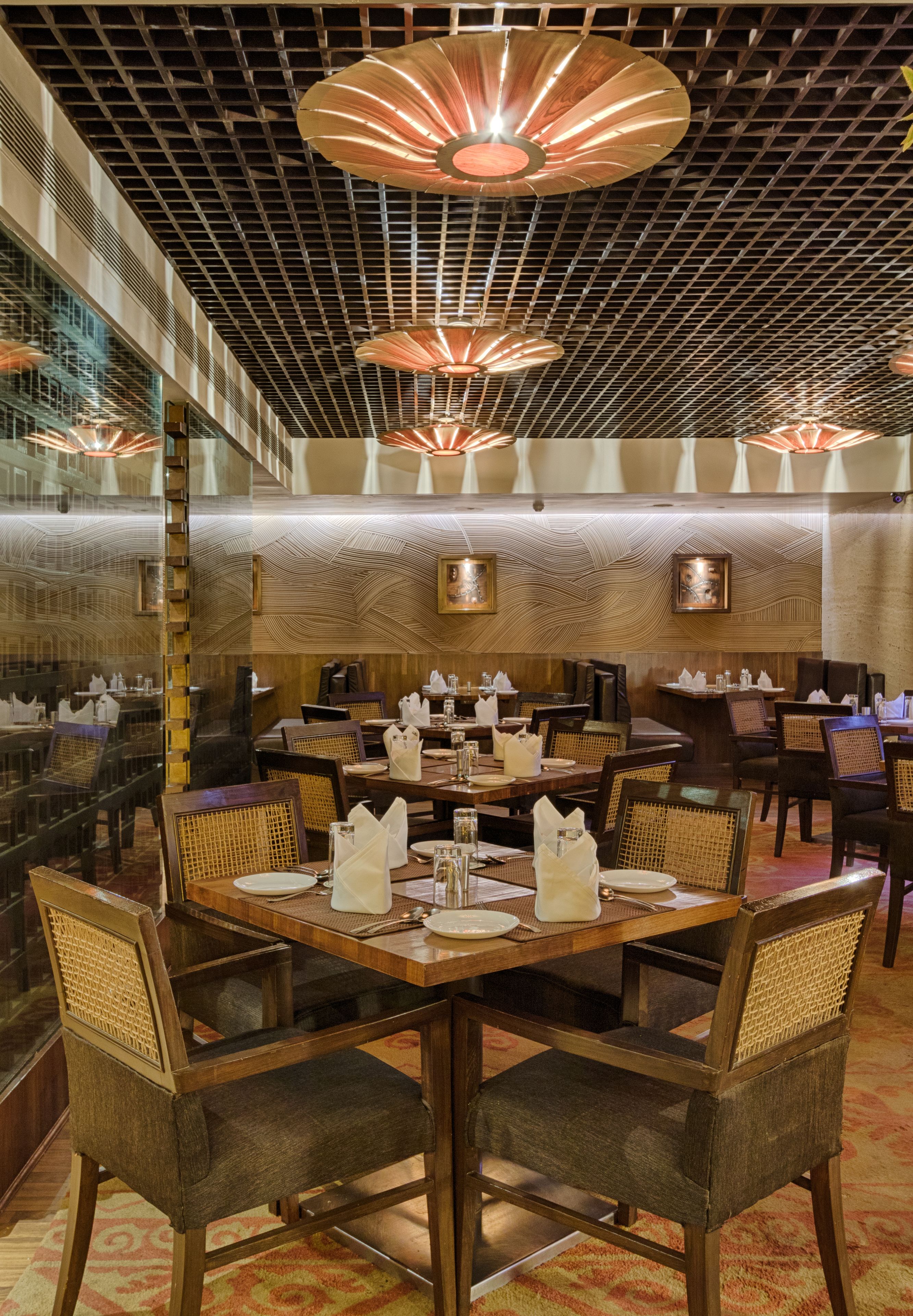A restaurant with round tables, wicker chairs, and a patterned ceiling.