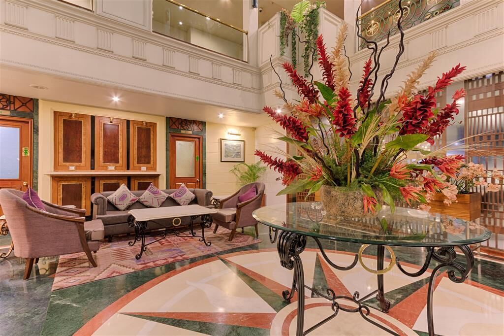 A lobby with a glass coffee table, seating area with sofas, and a decorative plant arrangement.