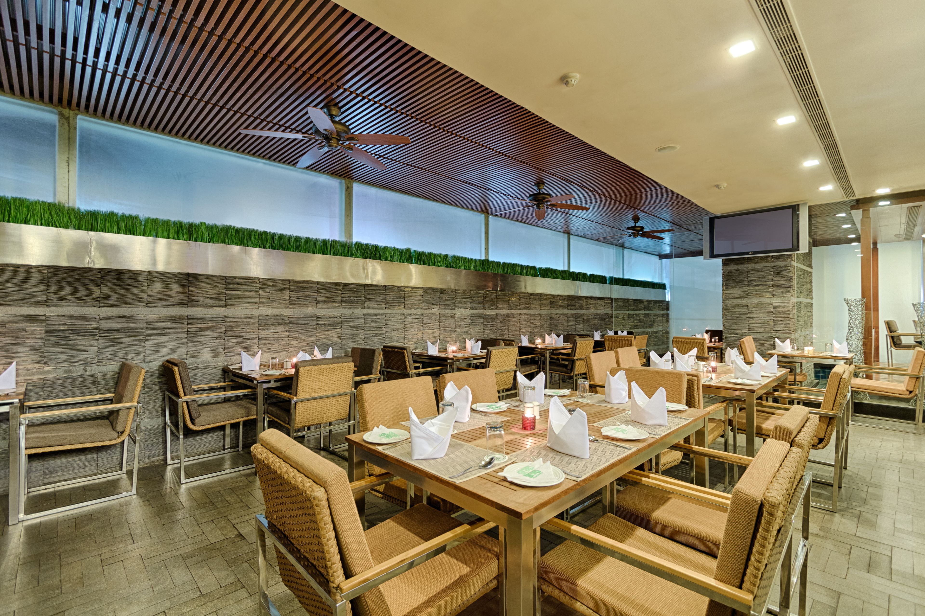 Un restaurante con varias mesas y sillas, ventiladores de techo y una pared con césped artificial.