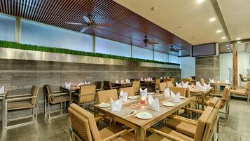 Un restaurante con varias mesas y sillas, ventiladores de techo y una pared con césped artificial.