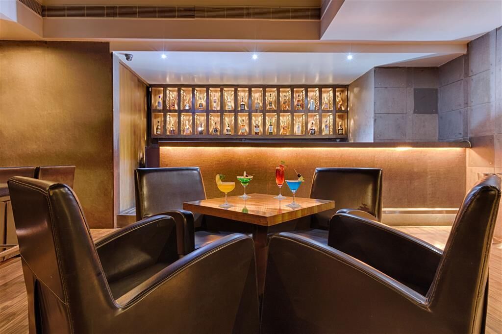 Un espace bar avec une table en bois et des fauteuils en cuir, un mur où sont accrochées des récompenses encadrées, et une lumière douce et chaleureuse.