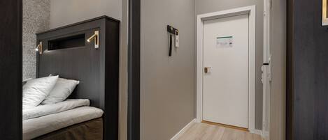 A narrow hallway with a bed on the left, a door with a sign on the right, and a bench on the right.