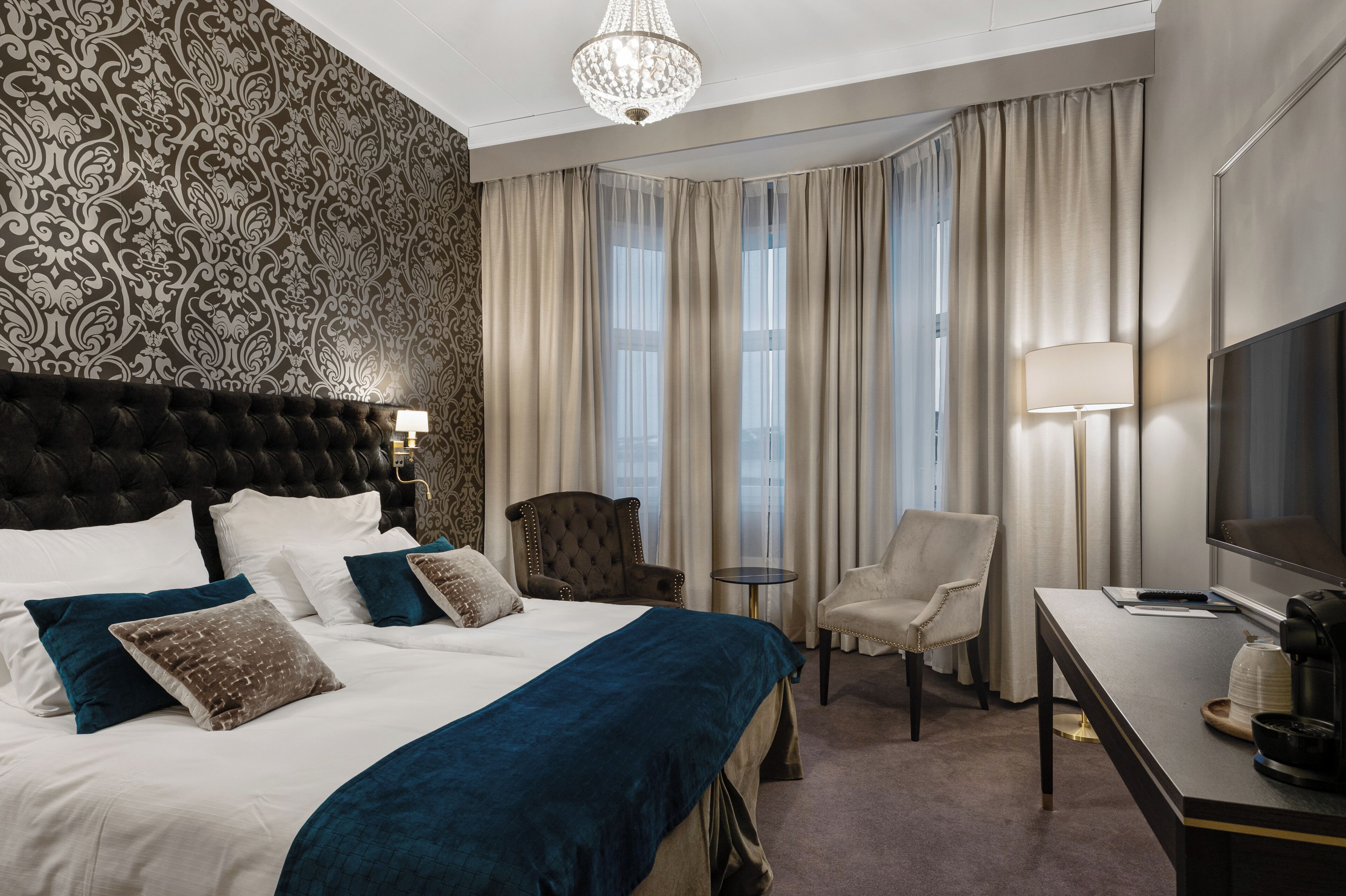 Une chambre d’hôtel avec un grand lit, un bureau, une chaise, une télévision et un lustre.