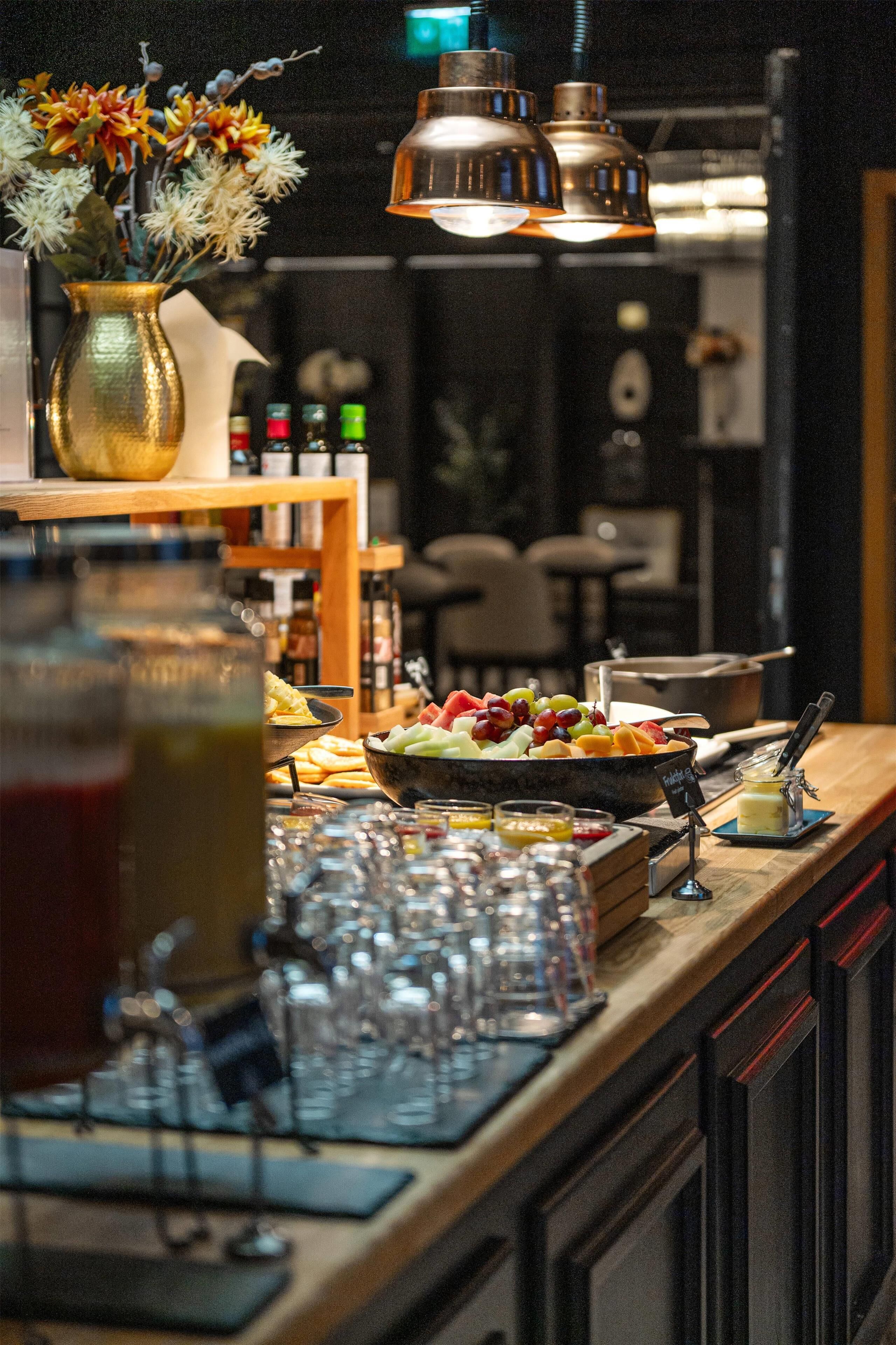 Un coin bar avec un panier de fruits, des verres et un vase de fleurs.