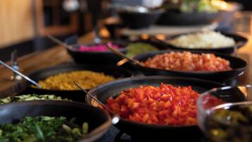 Un bufé con diversos platos, incluyendo tomates en cubos, verduras verdes y arroz.