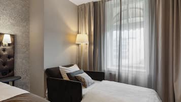 Habitación de hotel con dos camas, una mesita de noche, una lámpara y un ventanal con cortinas.