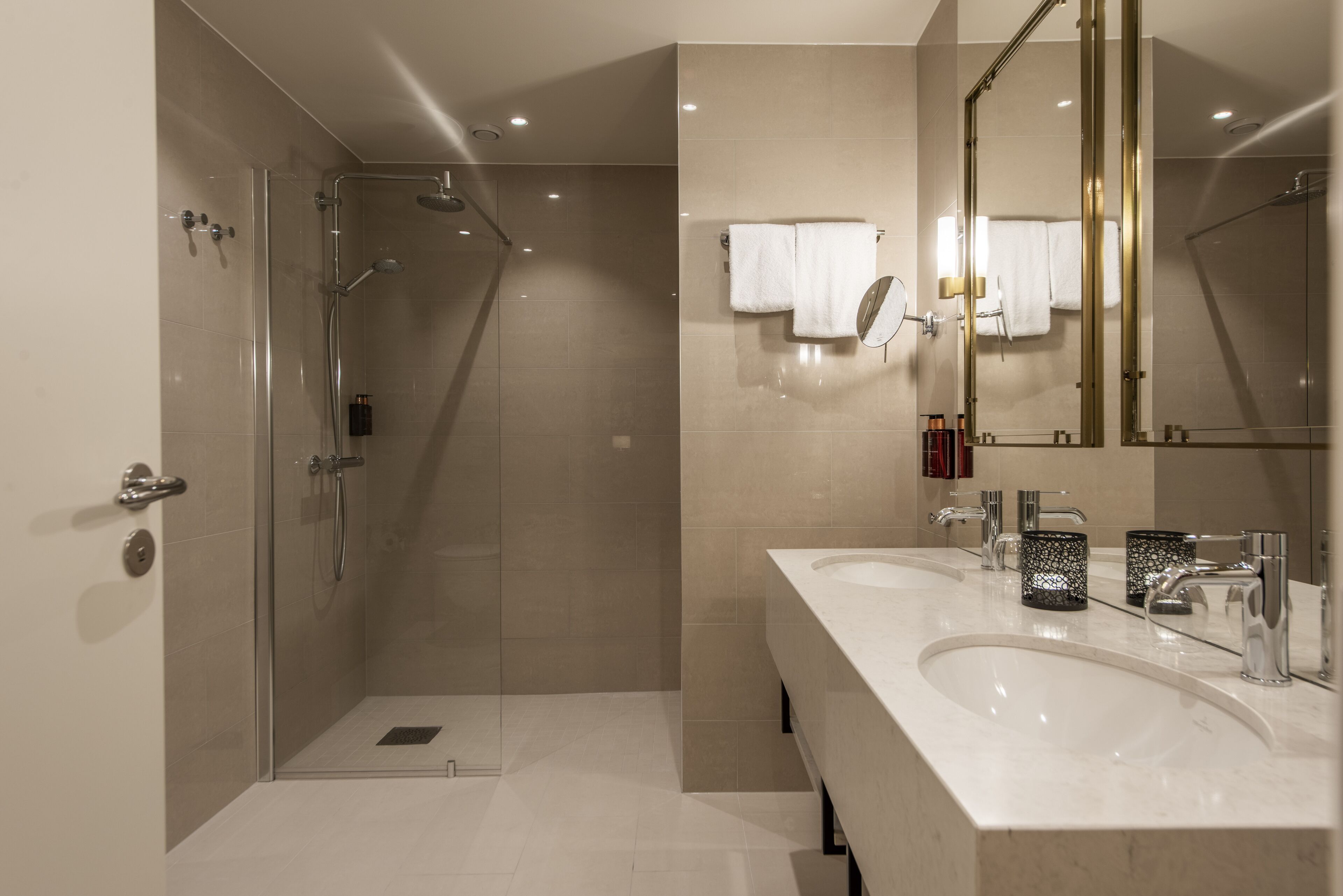 Un baño moderno con ducha acristalada, dos lavamanos y un espejo grande.