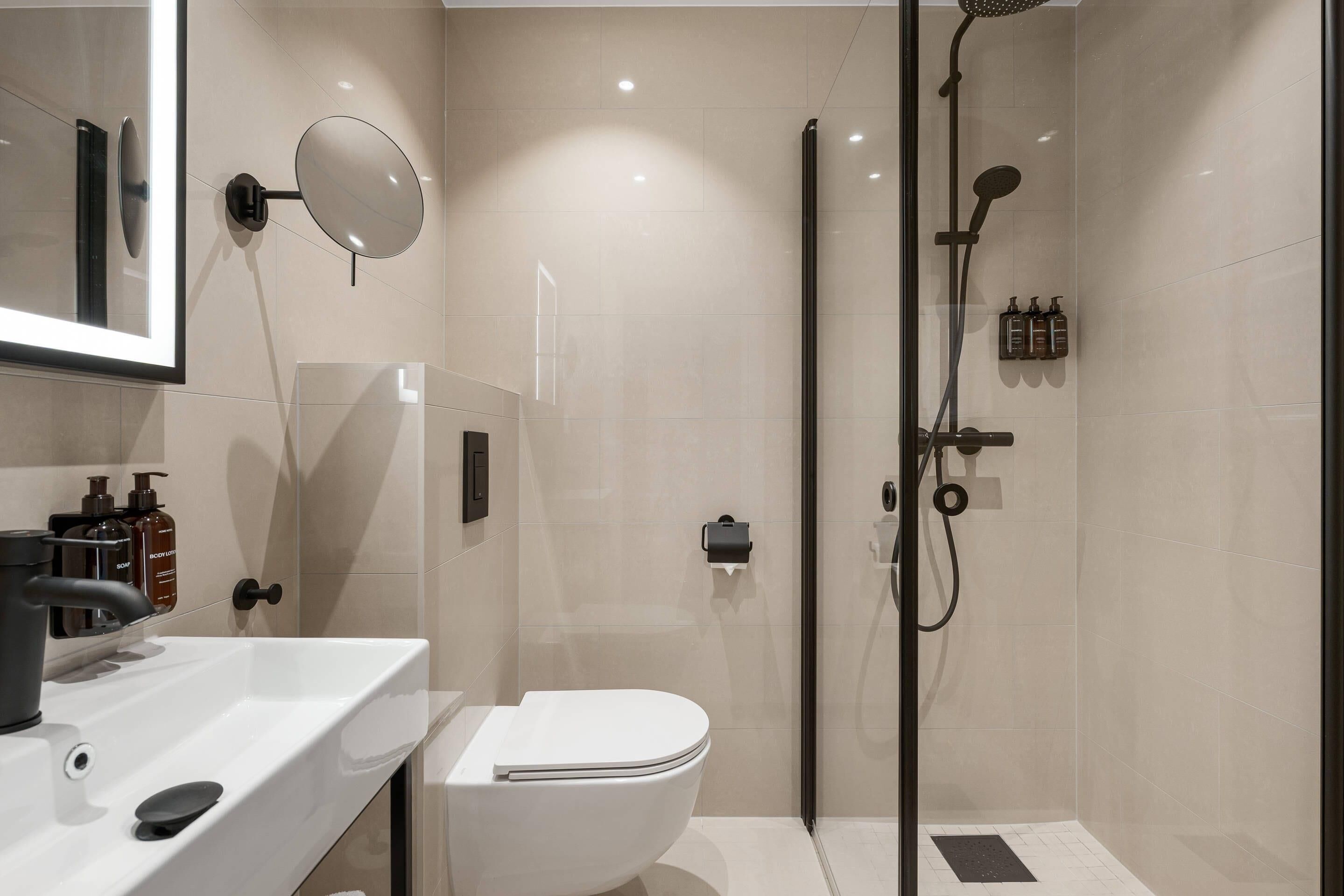 A modern bathroom with a toilet, sink, mirror, and shower.