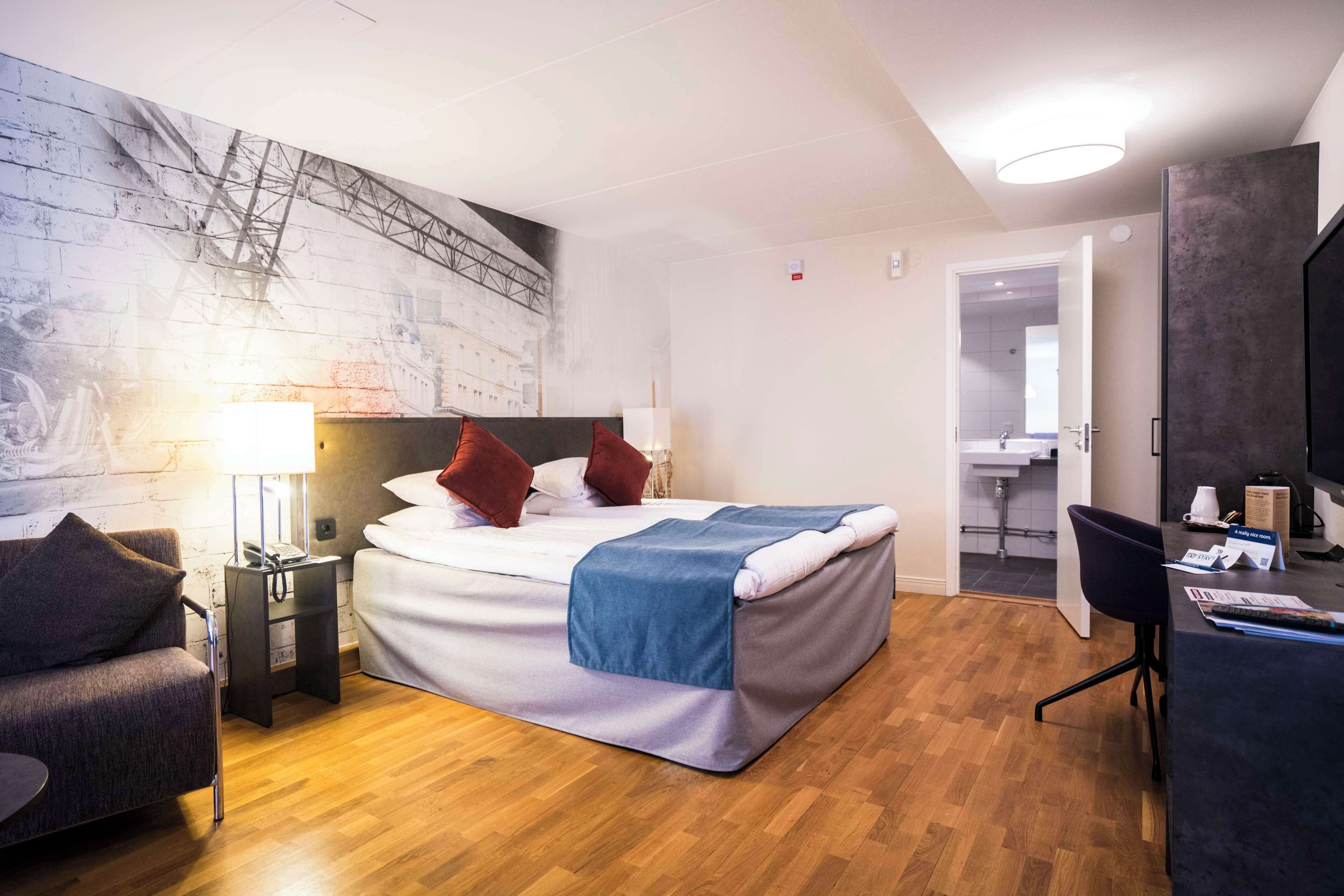 Una habitación de hotel moderna con una cama, un escritorio, una silla, una lámpara y una pared con un diseño estructural.