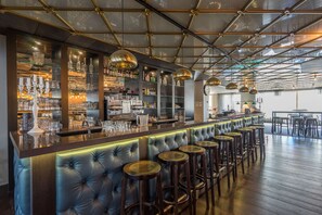 Zona de bar con una barra alargada, varios taburetes y una variedad de botellas y vasos en estantes.