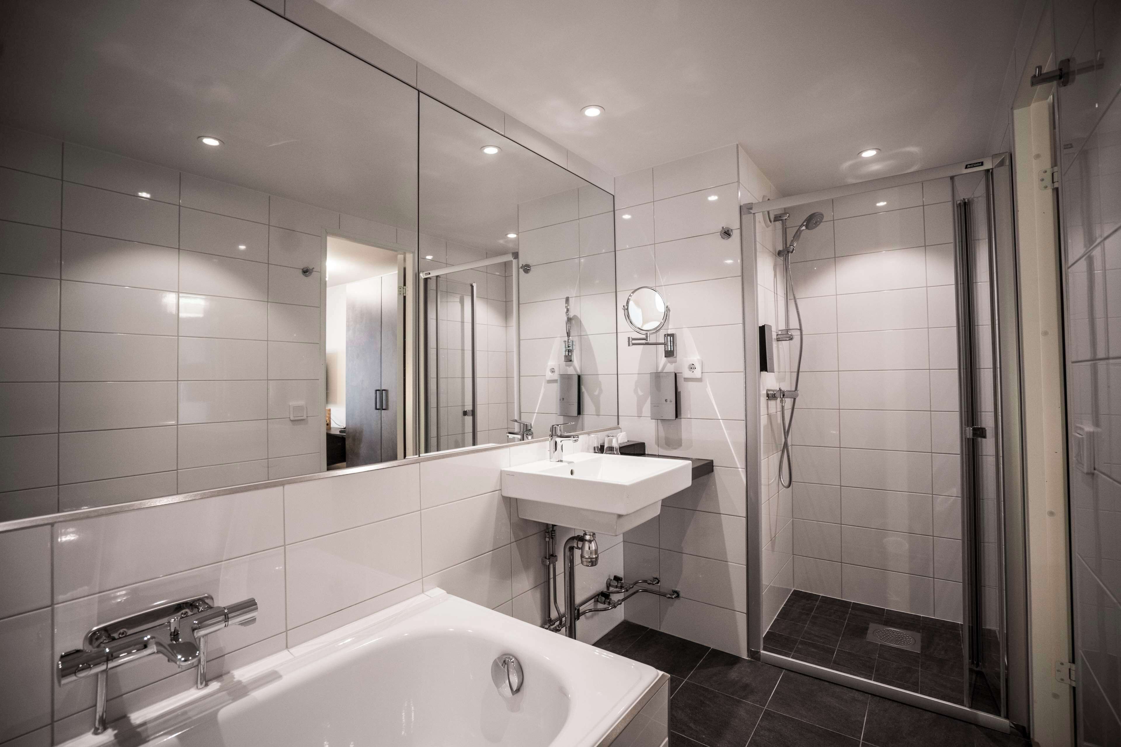 A modern bathroom with a large mirror, a bathtub, a shower, and a sink.