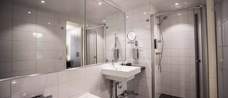 A modern bathroom with a large mirror, a bathtub, a shower, and a sink.