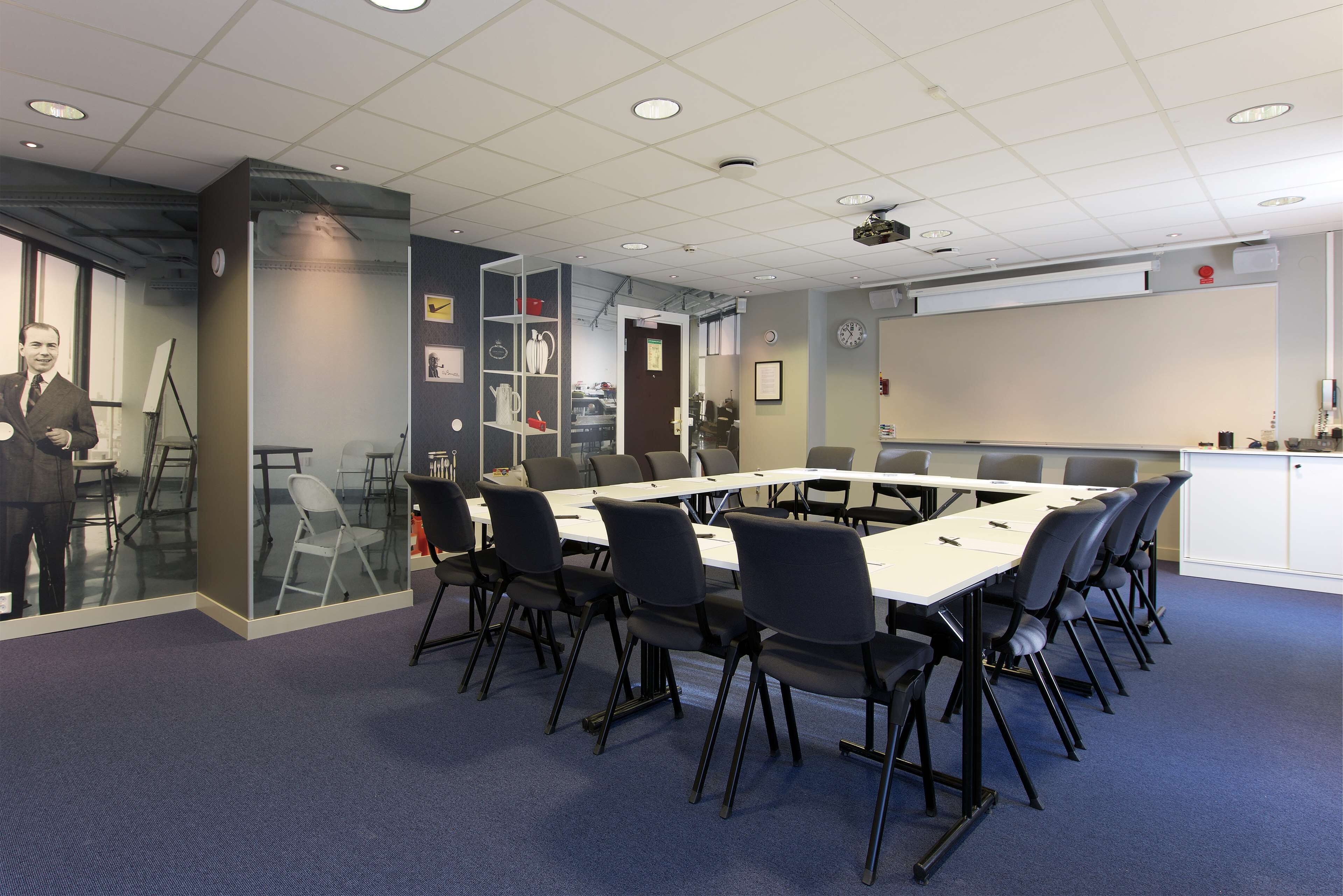Una sala conferenze con un lungo tavolo, sedie nere, una lavagna e un proiettore.