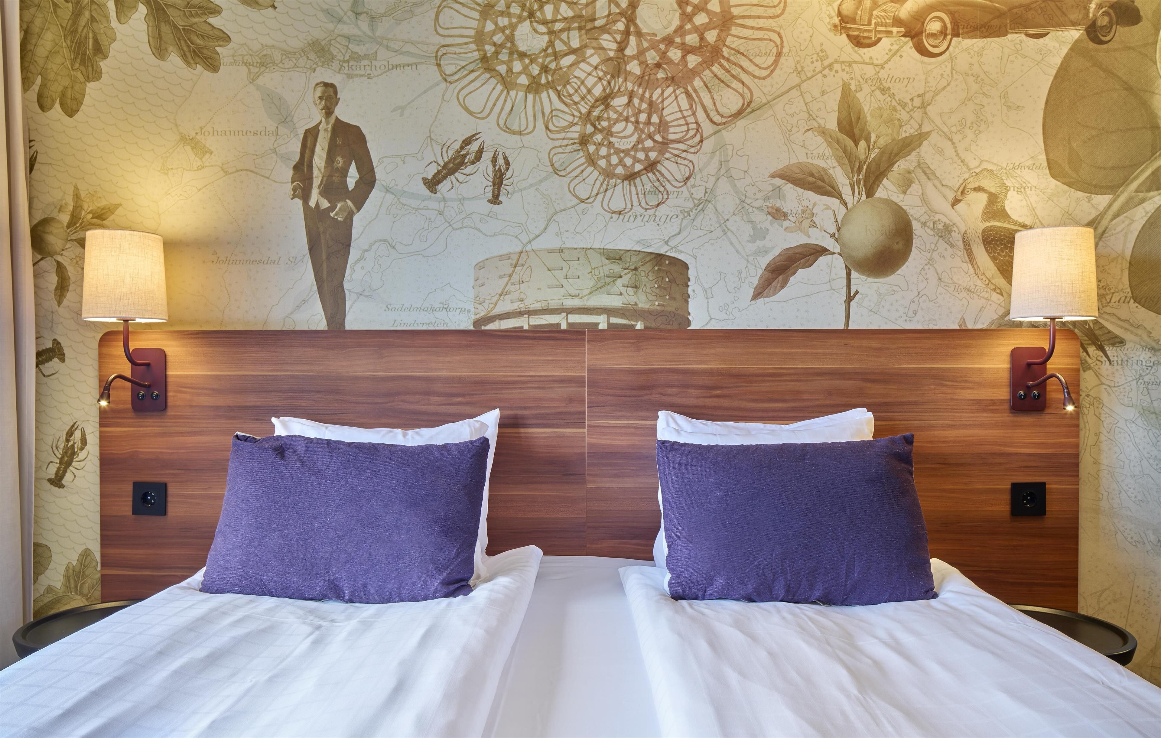 Uma cama de casal com roupa de cama branca e almofadas roxas, com duas luminárias fixadas na parede.