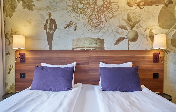 Cama doble con sábanas blancas y almohadas moradas, con dos lámparas fijadas a la pared.