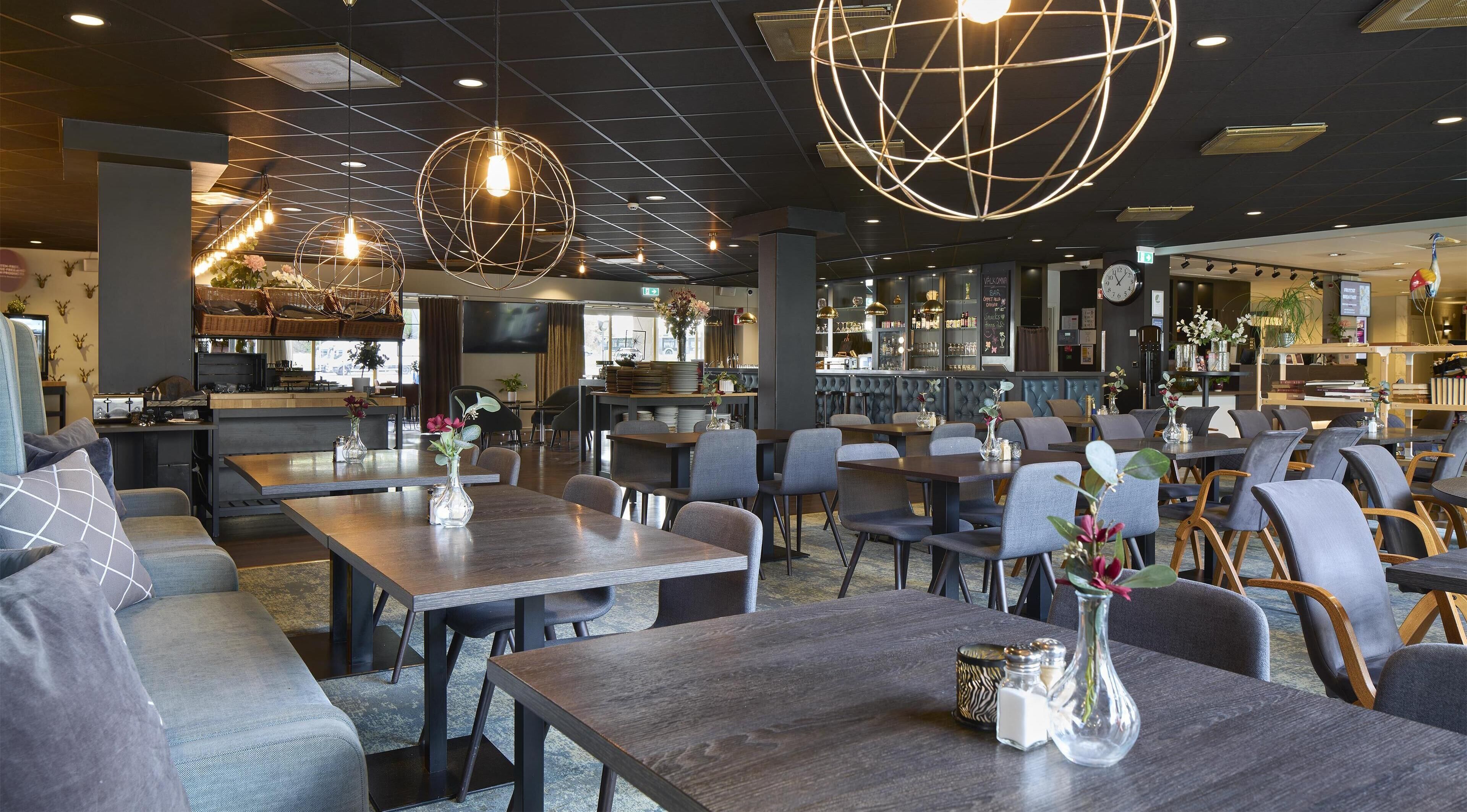 Un interior de restaurante moderno con varias mesas, sillas y lámparas esféricas colgantes.
